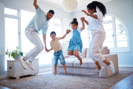 Photo for Young parents jumping and playing with their two children at home. Happy hispanic family having fun spending time together. Little boy and girl holding hands and jumping in the air with mom and dad. - Royalty Free Image