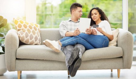 Téléchargez les photos : Qu'en penses-tu ? un couple utilisant une tablette numérique et une carte de crédit sur le canapé à la maison - en image libre de droit