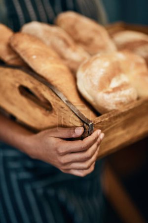 Foto de Donde hay un poco de mantequilla cuando la necesitas. una mujer sosteniendo una selección de panes recién horneados en su panadería - Imagen libre de derechos