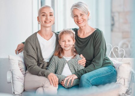 Téléchargez les photos : Three generations of females sitting together and looking at the camera. Portrait of an adorable little girl bonding with her mother and grandmother at home. Enjoying a visit with her granddaughter. - en image libre de droit