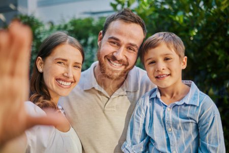 Photo for Family selfie in the garden at home. Young family of three snapping pictures while outside in the yard. Handsome man, beautiful woman and cute son taking photographs outside. - Royalty Free Image