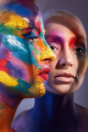 Foto de Me siento brillante. Foto de estudio de dos mujeres jóvenes posando con pintura multicolor en la cara - Imagen libre de derechos