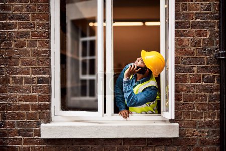 Foto de Veo el problema. un joven ingeniero hablando por su celular mientras mira por la ventana de una obra de construcción - Imagen libre de derechos