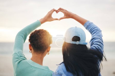 Photo for Love, beach and lesbian couple with heart hands at sunset, summer holiday adventure or date together. Lgbt women, bonding and relax on ocean vacation with romance, pride and happy partner in nature - Royalty Free Image