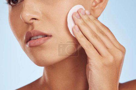 Photo for Woman, face and hands with cotton pad for skincare or makeup removal against a blue studio background. Closeup of female person with swab for foundation product, cosmetics or facial spa treatment. - Royalty Free Image