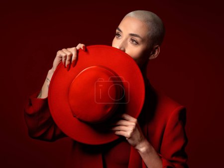 Photo for Vision, fashion and hat with a woman in studio on a red background for elegant or trendy style. Thinking, hide and cover with a young female model looking edgy or classy in a suit for beauty. - Royalty Free Image