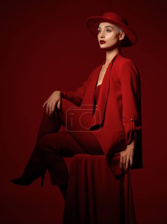 Photo for Thinking, fashion and a woman sitting on a red studio background for elegant or trendy style. Vision, art and beauty on a chair with a young female model looking edgy or classy in suit clothes. - Royalty Free Image