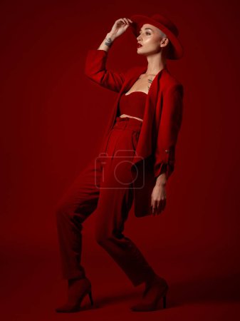 Photo for Art, fashion and a model woman on a red studio background for elegant or trendy style. Aesthetic, beauty and bold with a young female person looking edgy or classy in a suit walking on the runway. - Royalty Free Image