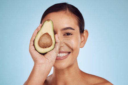 Photo for Avocado, eye skincare and woman in portrait for healthy face or natural cosmetics on studio blue background. Happy person or model of green fruits, vitamin d benefits and dermatology or beauty health. - Royalty Free Image