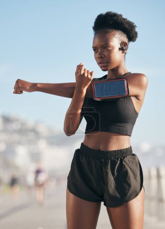 Photo for Thinking, music and stretching with a sports black woman outdoor on a blurred background for cardio or endurance training. Fitness, exercise and phone with a young athlete getting ready for a workout. - Royalty Free Image