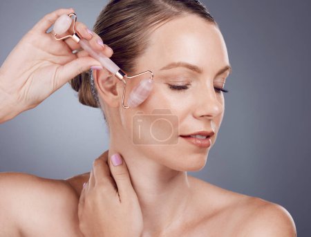 Photo for Rose quartz, facial massage and woman with face roller for wellness, dermatology and skincare. Isolated, gray background and model with beauty for facelift and self care with crystal in studio. - Royalty Free Image