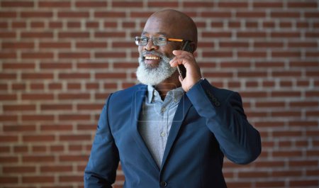 Téléchargez les photos : Appel téléphonique de l'homme d'affaires noir sur le mur de briques pour la communication, le succès du réseautage ou des nouvelles. Heureux gestionnaire professionnel, cadre supérieur ou patron parlant sur smartphone pour une opportunité d'investissement. - en image libre de droit