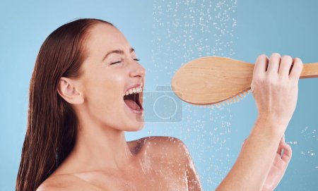 Foto de Mujer feliz, ducha y canto con cepillo para la higiene, limpieza o amor propio y cuidado corporal sobre un fondo de estudio azul. Persona femenina disfrutando de agua, lluvia o lavado para su limpieza o aseo. - Imagen libre de derechos