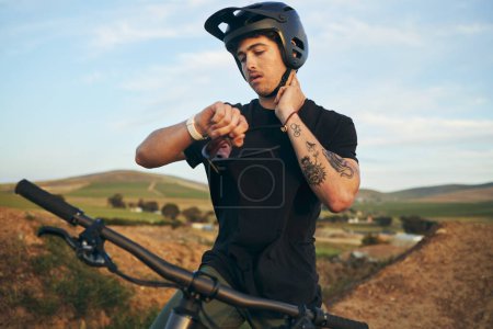 Photo for Sports, bike and man checking his pulse on a mountain dirt road in nature for race or competition training. Fitness, exercise and young male biker athlete with watch for the time at an outdoor trail - Royalty Free Image