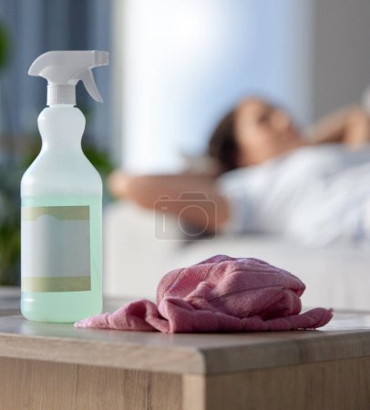 Photo for Cleaning, covid or hygiene with supplies in a house with a woman cleaner taking a break in the background. Home, product and housekeeping with a spray, disinfectant or sanitizer for health and safety. - Royalty Free Image