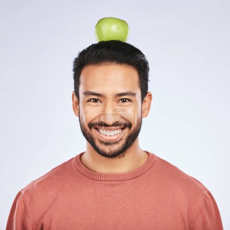 Photo for Portrait, apple head balance and man smile for weight loss diet, healthy snack or body nutrition vitamins. Eating food, nutritionist fruit and studio face of hungry Asian person on white background. - Royalty Free Image
