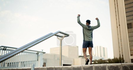 Photo for Man, fitness and celebration in city with fist pump for achievement, workout or success in outdoor exercise. Rear view of male person, runner or athlete with hands up in victory for training in town. - Royalty Free Image