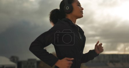 Photo for Fitness, music and a woman running in the city for health or cardio preparation of a marathon. Exercise, wellness or sports training and a young runner or athlete listening to audio with headphones. - Royalty Free Image