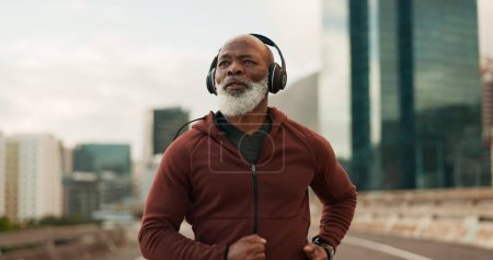 Photo for Mature, athlete and running in city with headphones for fitness, workout or marathon training music. Black man, thinking or exercise podcast in South Africa for cardio wellness, health or sport radio. - Royalty Free Image