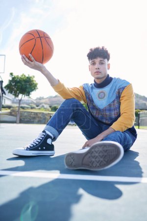 Photo for Basketball, court and portrait of a man model sitting on the ground with stylish, trendy and cool clothes. Sports, relax and guy from Canada holding a ball on outdoor training field in the urban city. - Royalty Free Image