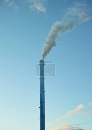 Téléchargez les photos : Une cheminée d'usine avec de la fumée soufflant dans l'air. Grande quantité de vapeur ou de fumée provenant d'une cheminée industrielle, ce qui ajoute à la pollution et à la contamination de l'air provenant des grandes industries industrielles. - en image libre de droit