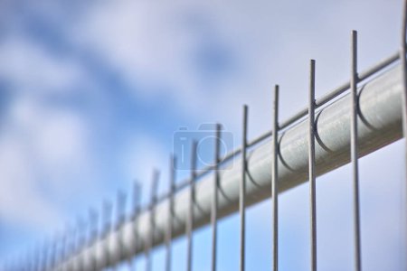 Photo for Closeup of a new metal fence against a cloudy blue sky. Safety and security to protect your home and property. Sharp spikes to keep people out. Constructing a fence or cage. Danger keep out. - Royalty Free Image
