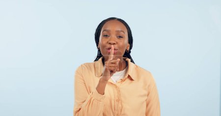 Photo for Black woman, whisper or finger on lips for secret, gossip or confidential information on blue background. Studio, portrait and person sign for quiet, hush or privacy emoji for surprise announcement. - Royalty Free Image