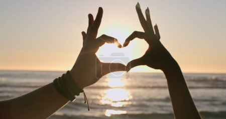 Photo for Love, hands and heart on beach with sunset, water background and horizon for vacation, travel or adventure. People, man and woman by ocean or sea with emoji for romance, care and relationship on trip. - Royalty Free Image