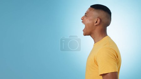 Photo for Angry, man and scream in studio at mockup space for crisis, anger or mad emoji reaction on blue background. Profile of frustrated model shouting with stress, emotional conflict or negative expression. - Royalty Free Image