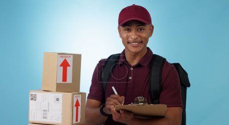 Photo for Delivery man, boxes and checklist for courier service, distribution and writing invoice on a blue background. Portrait of logistics worker with package, receipt and clipboard or paperwork in studio. - Royalty Free Image