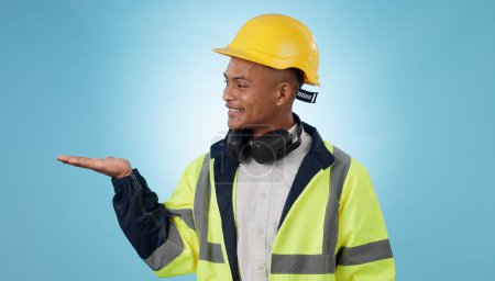 Photo for Construction worker, smile and with hand for advertising, promotion or mockup in blue background. Happy, face and builder show safety announcement, presentation or choice with space in studio. - Royalty Free Image