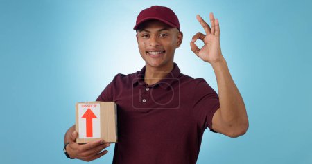 Photo for Delivery man, box and okay hands for success, product excellence and courier services in studio. Happy portrait of supply chain worker or person with package for distribution on a blue background. - Royalty Free Image