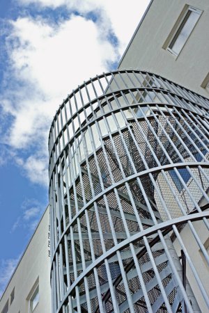 Photo for A spiral staircase on the outside of a building. Grey steel spiral stairs built on the side of modern industrial office building. Low angle of a metal circular fire escape staircase with railings. - Royalty Free Image