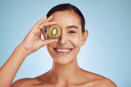 Photo for Beauty portrait, kiwi and woman with eye skincare, cosmetics and natural product, health and vitamin c. Face of young happy person or model, green fruits and dermatology on a studio, blue background. - Royalty Free Image