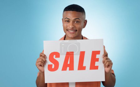 Photo for Portrait, sale sign or happy man by offer, discount deal or launch for poster or business advertising. Show, smile or person with board for message, marketing or promotion card on blue background. - Royalty Free Image
