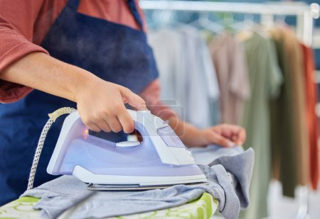 Photo for Closeup of a female maid ironing clothes on a board in the laundry room of a modern house. Cleaning, chores and zoom of a woman cleaner or housewife steaming washing with an iron in an apartment - Royalty Free Image
