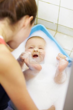 Photo for Baby, mother or play in bathtub for shower, cleaning and hygiene with foam or bubbles for bonding. Child, woman or washing infant in bathroom of home for parenting, development and love with water. - Royalty Free Image