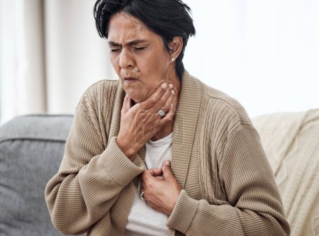 Senior woman, cough and sick on sofa in home, chest pain and pneumonia with tuberculosis or choke. Pensioner, mature lady or sore throat with lung infection, breathing problem and choking with asthma.