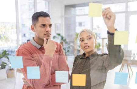 Photo for Creative people, planning and thinking for schedule, team strategy or brainstorming on glass wall at office. Man and woman in teamwork contemplating plan, tasks and post it for sticky note or startup. - Royalty Free Image