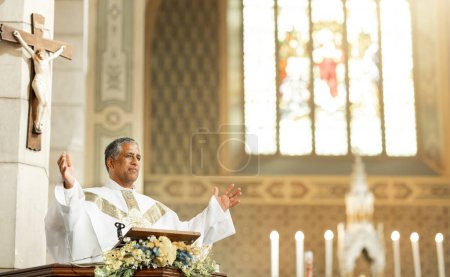 Photo for Religion, Christianity and priest speaking in church with arms raised standing by podium. Ceremony, mass and religious leader in worship, preaching and prayer for congregation in spiritual building. - Royalty Free Image