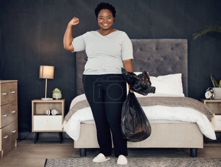 Foto de Mujer negra, bolsa de basura y campeona, éxito en limpieza y dormitorio con higiene en retrato. Limpiadora femenina fuerte, ganadora en limpieza con sonrisa, rutina matutina y mantenimiento en casa. - Imagen libre de derechos