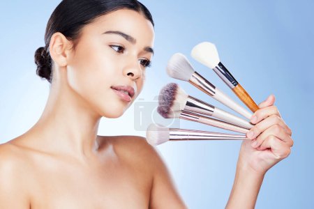 Photo for Makeup, beauty and woman with brushes in hand on blue background for cosmetics, powder and foundation. Cosmetology, salon aesthetic and face of girl with tools for application, wellness and glow. - Royalty Free Image