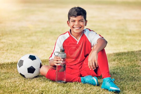 Photo for Soccer, children and water with a ball and boy child sitting on a grass pitch or field after training. Football, fitness and hydration with a young male kid at a sports venue, stadium or arena. - Royalty Free Image