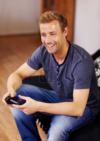 Photo for Man, video game and home on sofa, controller or smile for online competition, relax or press in lounge. Gamer person, playing and idea with click for strategy, streaming or digital challenge on couch. - Royalty Free Image
