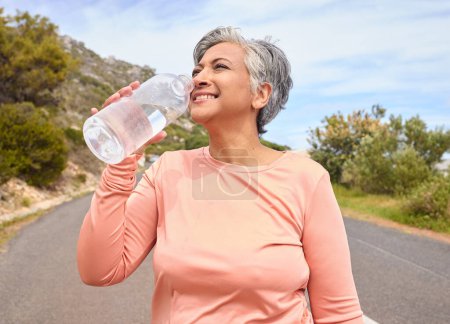 Photo for Senior woman, drinking water and bottle on road for fitness, running and thinking of goal, hydration or health. Mature lady, runner and detox with smile for wellness, exercise or workout in nature. - Royalty Free Image