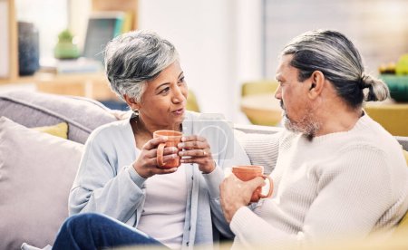 Photo for Coffee, conversation and senior couple on a sofa for bond, discussion or sharing gossip in their home. Love, tea and old people relax on couch for break, speaking or did you know drama in living room. - Royalty Free Image