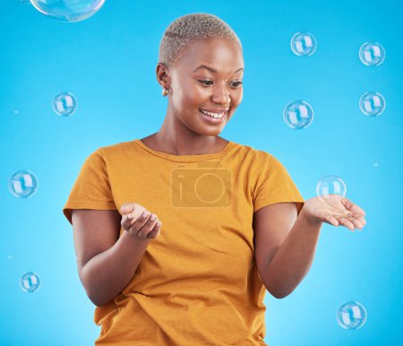 Téléchargez les photos : Femme noire, jouant avec des bulles et le bonheur, amusant et vibrant avec divertissement sur fond bleu. Savon liquide, la liberté et la femme africaine, ludique avec l'activité et profiter en studio. - en image libre de droit