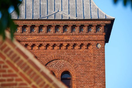 Photo for Closeup of a red face brick church steeple against a blue sky. Tall infrastructure and tower used to symbolise faith and Christian or Catholic devotion. Architecture of a built structure outside. - Royalty Free Image