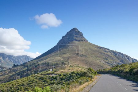Téléchargez les photos : Une route menant à Lions Head au Cap, en Afrique du Sud, contre le ciel bleu copyspace par une matinée ensoleillée. Une autoroute le long d'un paysage montagneux paisible avec des vues panoramiques ou des buissons et des arbres verdoyants. - en image libre de droit