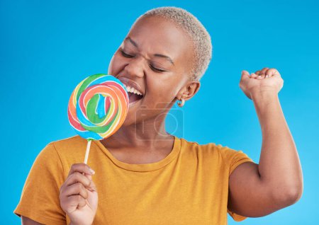 Foto de Piruleta, canto y una mujer con caramelos en estudio para dulces, arco iris y publicidad creativa. Mujer negra feliz aislada sobre un fondo azul con azúcar, libertad y felicidad o color. - Imagen libre de derechos